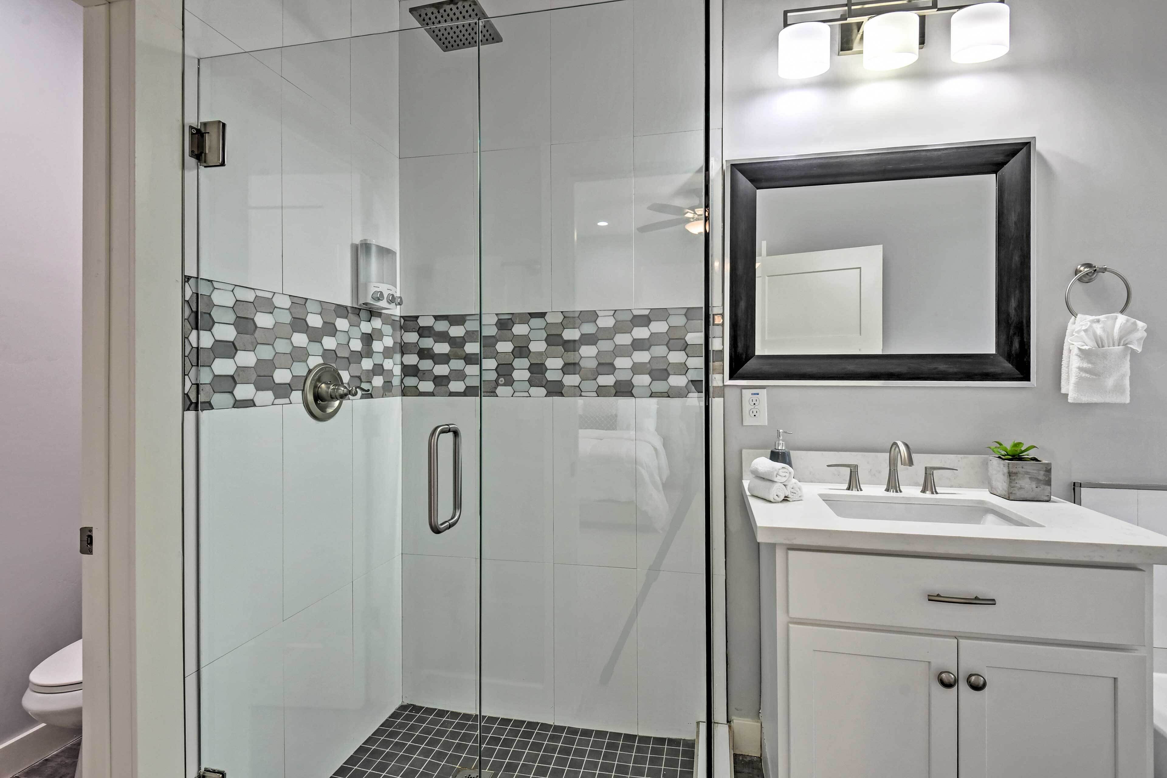 A modern bathroom with a glass-enclosed shower, a white sink with a mirror, and a tiled backsplash.