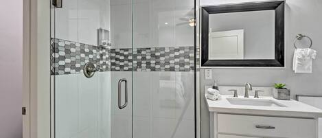 A modern bathroom with a glass-enclosed shower, a white sink with a mirror, and a tiled backsplash.