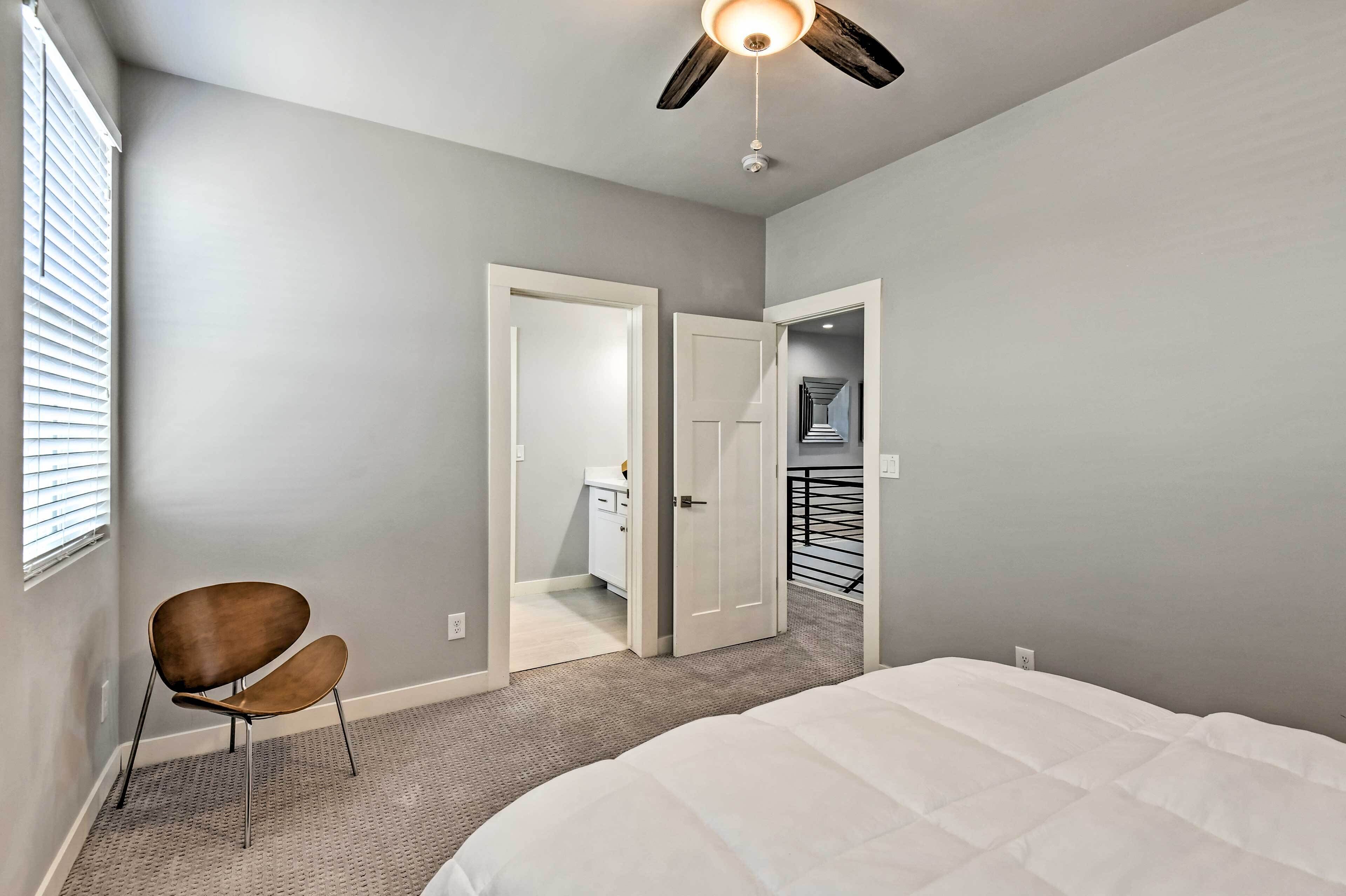 A bedroom with a bed, a chair, a ceiling fan, and a door leading to a bathroom.