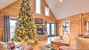 A cozy log cabin interior with a large Christmas tree, leather sofas, a fireplace, and wooden walls.
