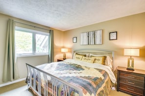A bedroom with a bed, two bedside tables, a window with curtains, and wall art.