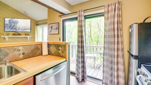 A kitchen with a wooden countertop, stainless steel sink, and a refrigerator. There is a window with a view of trees and a balcony with a checkered curtain. - Second-floor Condo w/ Community Pool Access! (Nellysford)