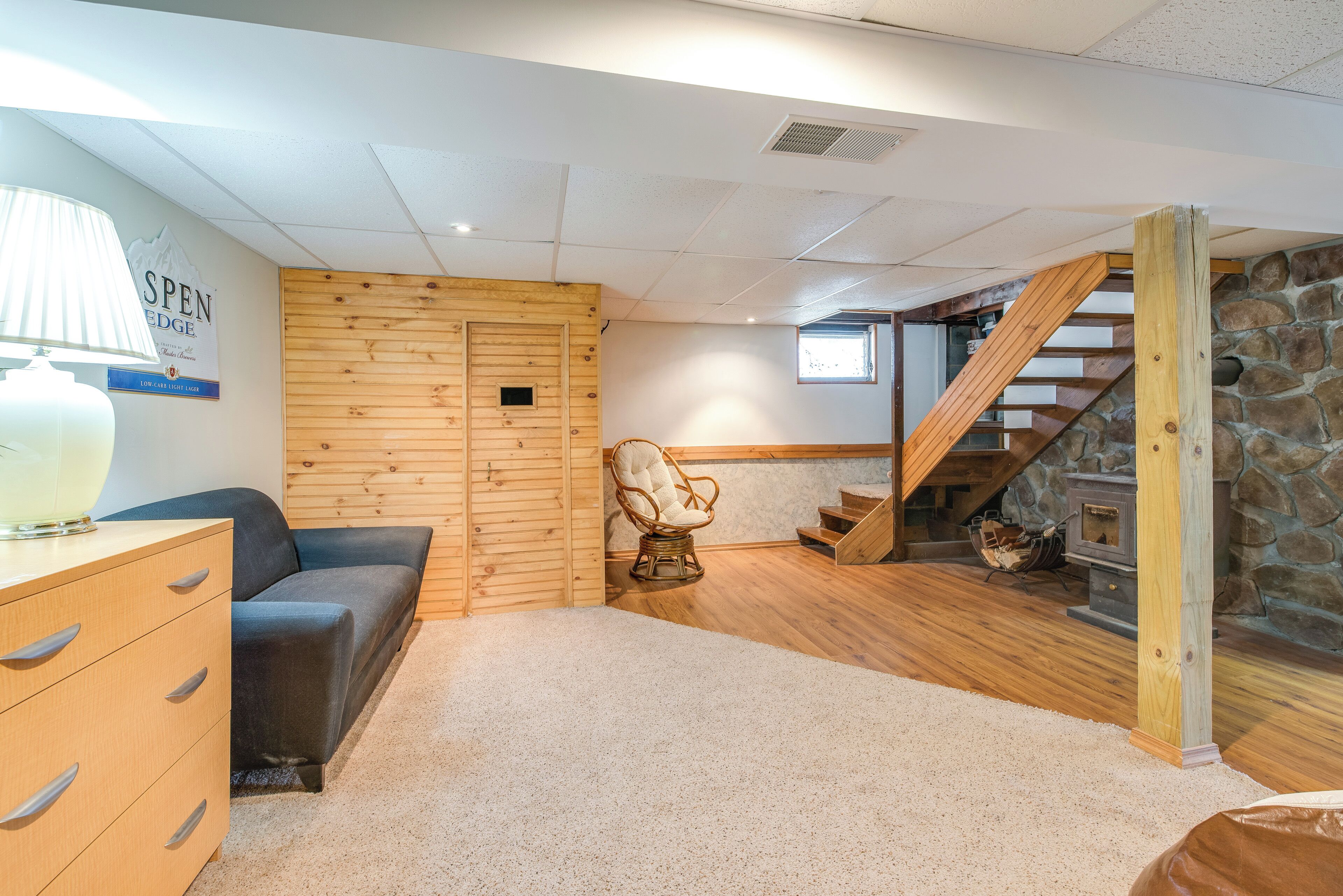 Una habitación acogedora con una pared de madera, un sillón cómodo, un sofá, una escalera de madera y una chimenea.