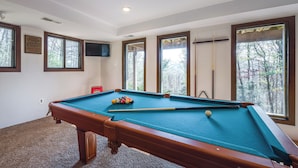 A pool table in a room with large windows and a mounted television.