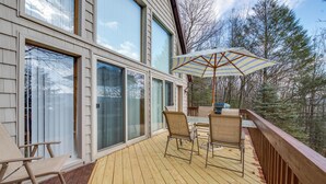 A wooden deck with two chairs and a table, a large umbrella, and a view of trees.