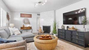 Ein modernes Wohnzimmer mit einem grauen Sofa, einem runden gewebten Couchtisch, einer schwarzen Kommode und einem flachbildfernseher, der an der Wand montiert ist.