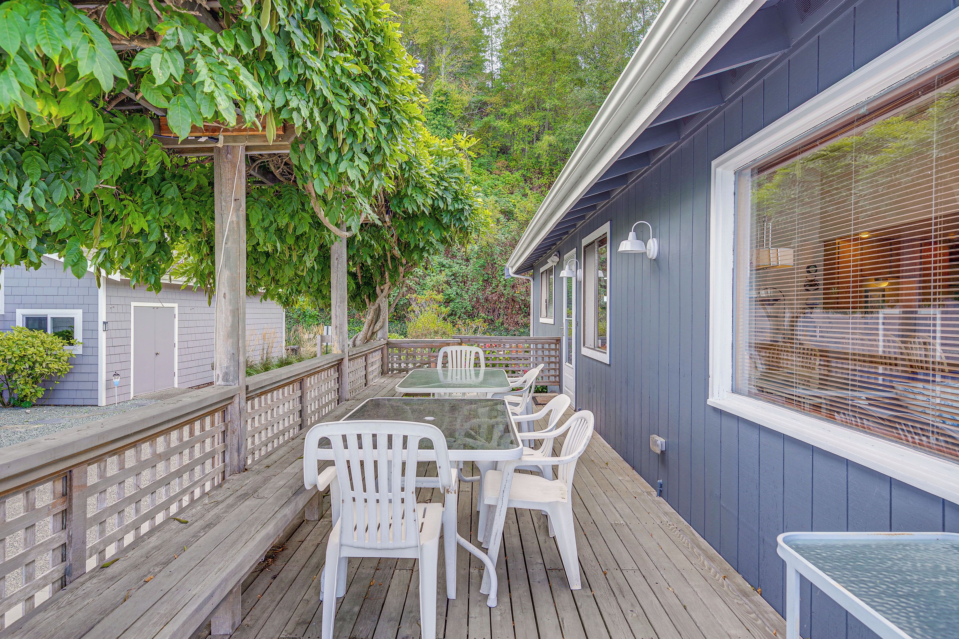 A covered deck with a table and chairs, surrounded by a wooden railing and a pergola with climbing plants.