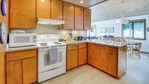 A kitchen with wooden cabinets, a white stove, and a microwave. There is a dining area with a table and chairs.