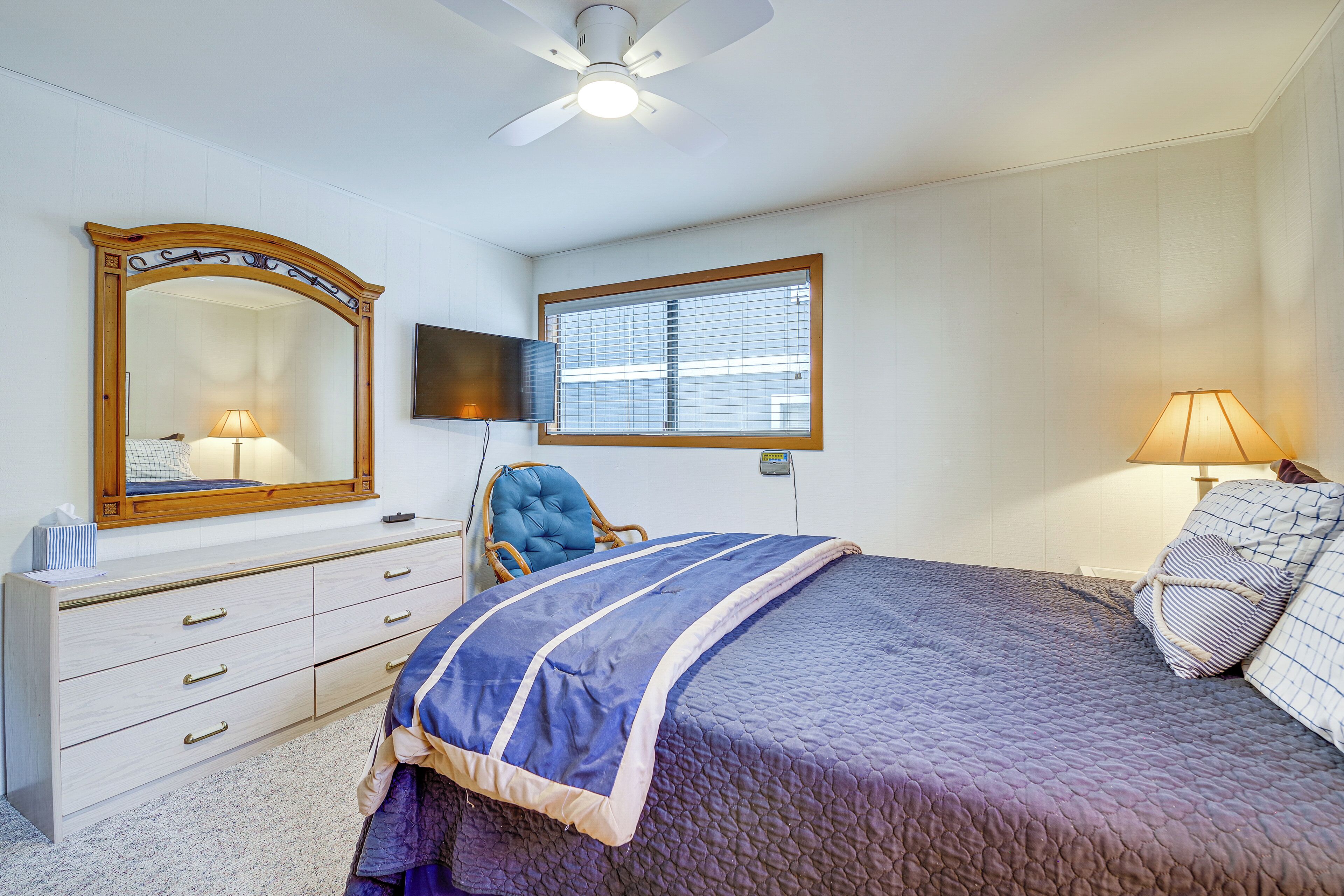 A bedroom with a bed, a dresser, a chair, a television, a window, and a ceiling fan.
