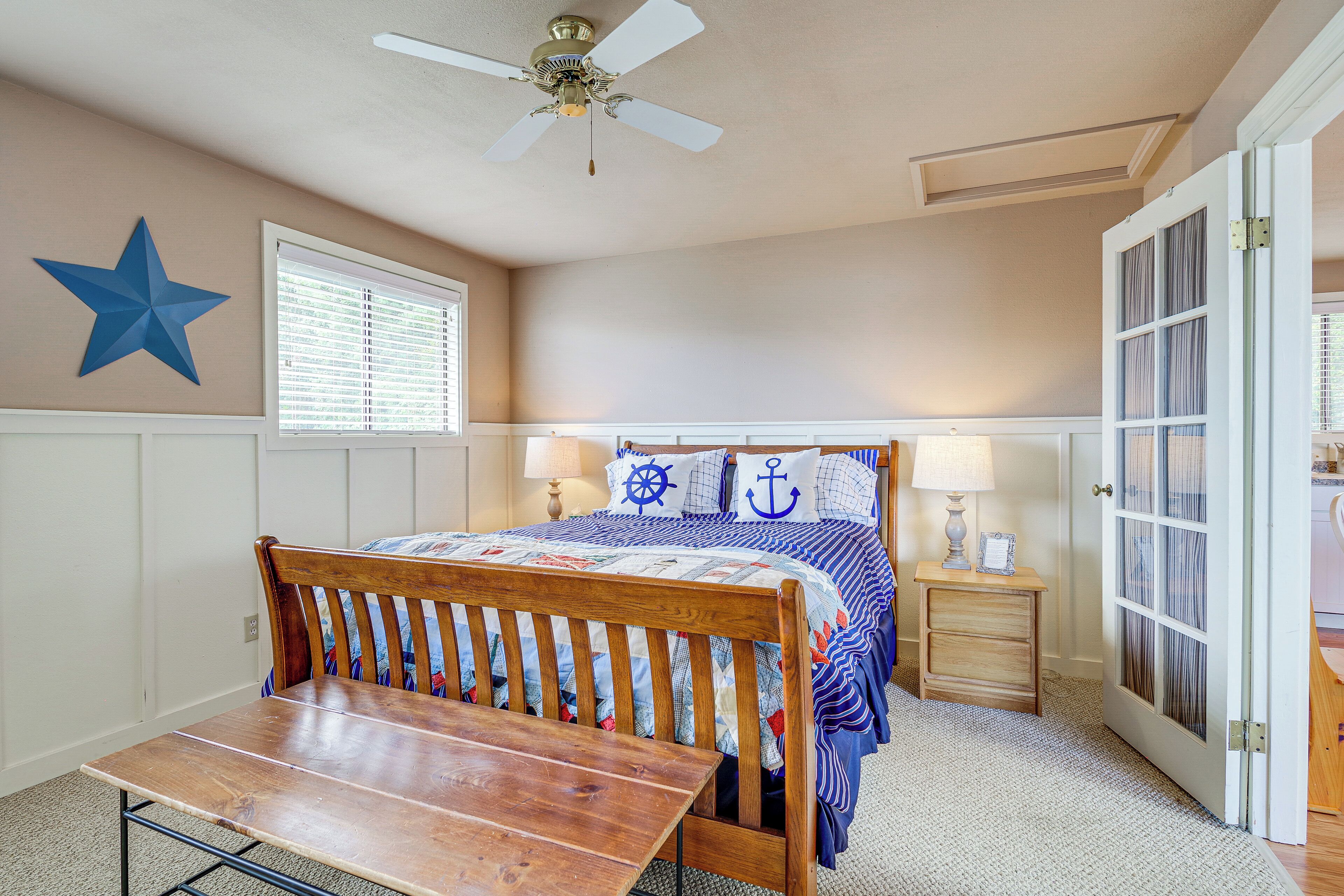Une chambre avec un lit, un banc en bois, un ventilateur de plafond, une décoration en forme d’étoile, une fenêtre avec des stores et une porte avec des panneaux de verre.