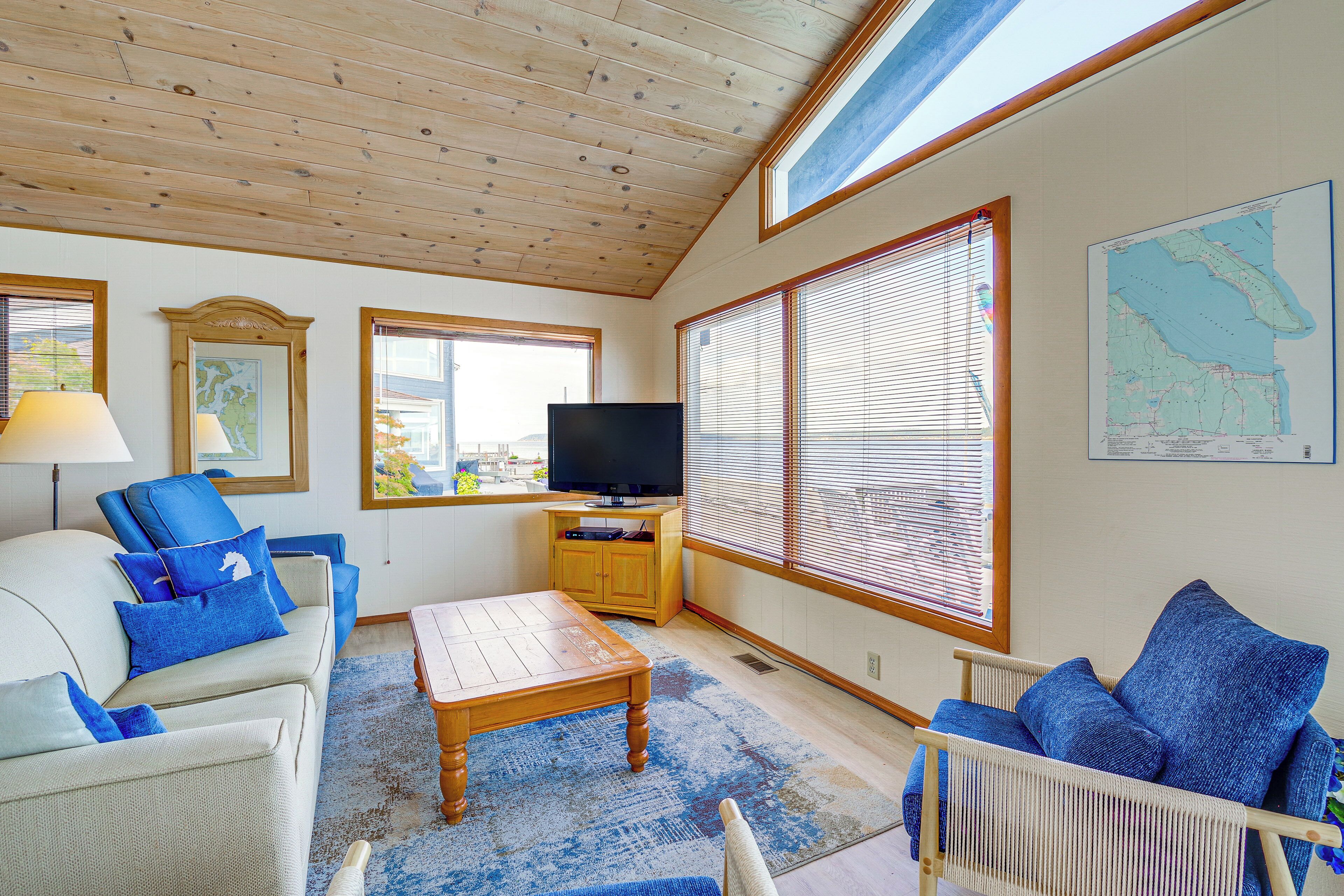A living room with a wooden ceiling, a television on a wooden stand, a sofa with blue cushions, a coffee table, and a chair.