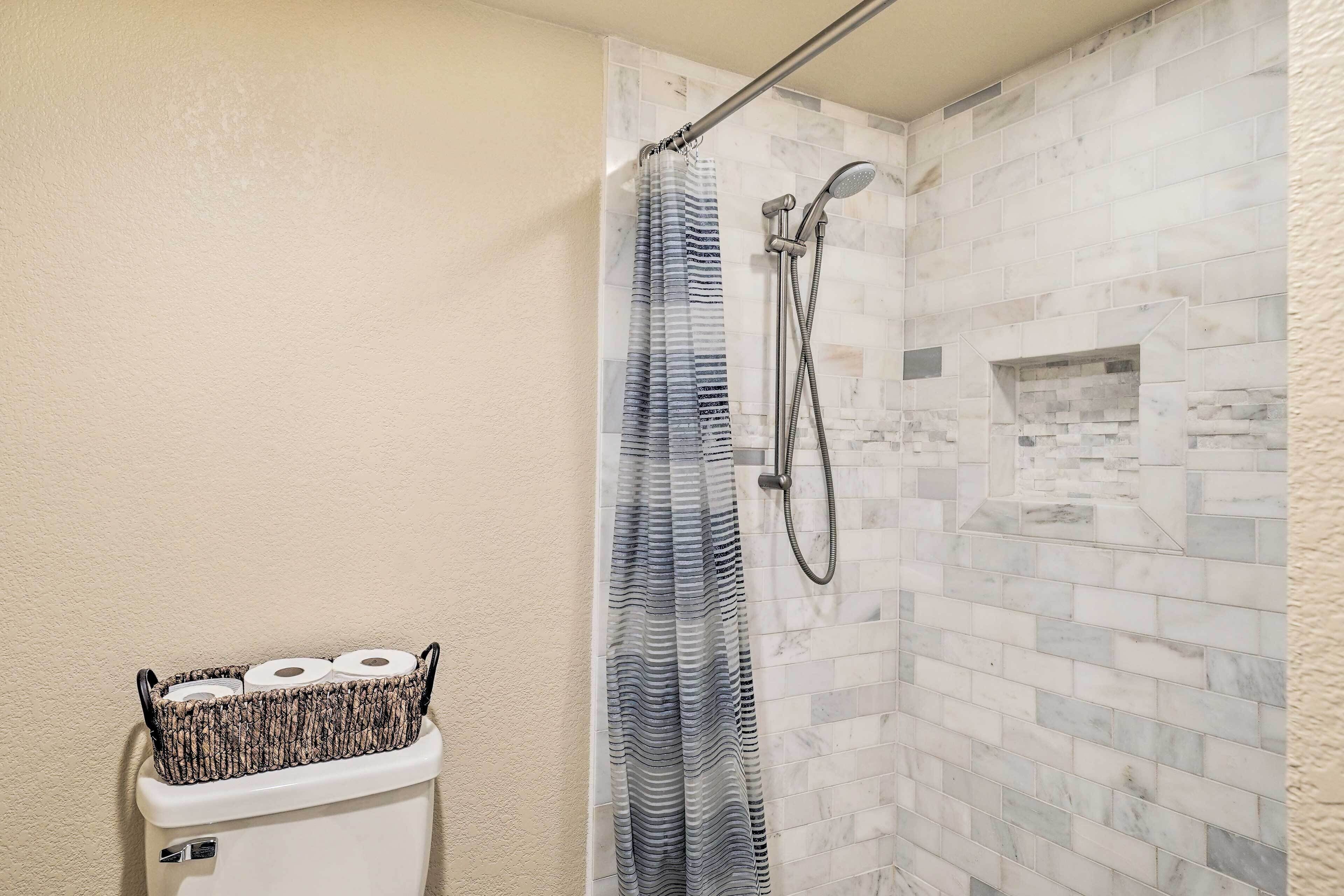 A bathroom with a shower, toilet, and a basket of toilet paper on the wall.