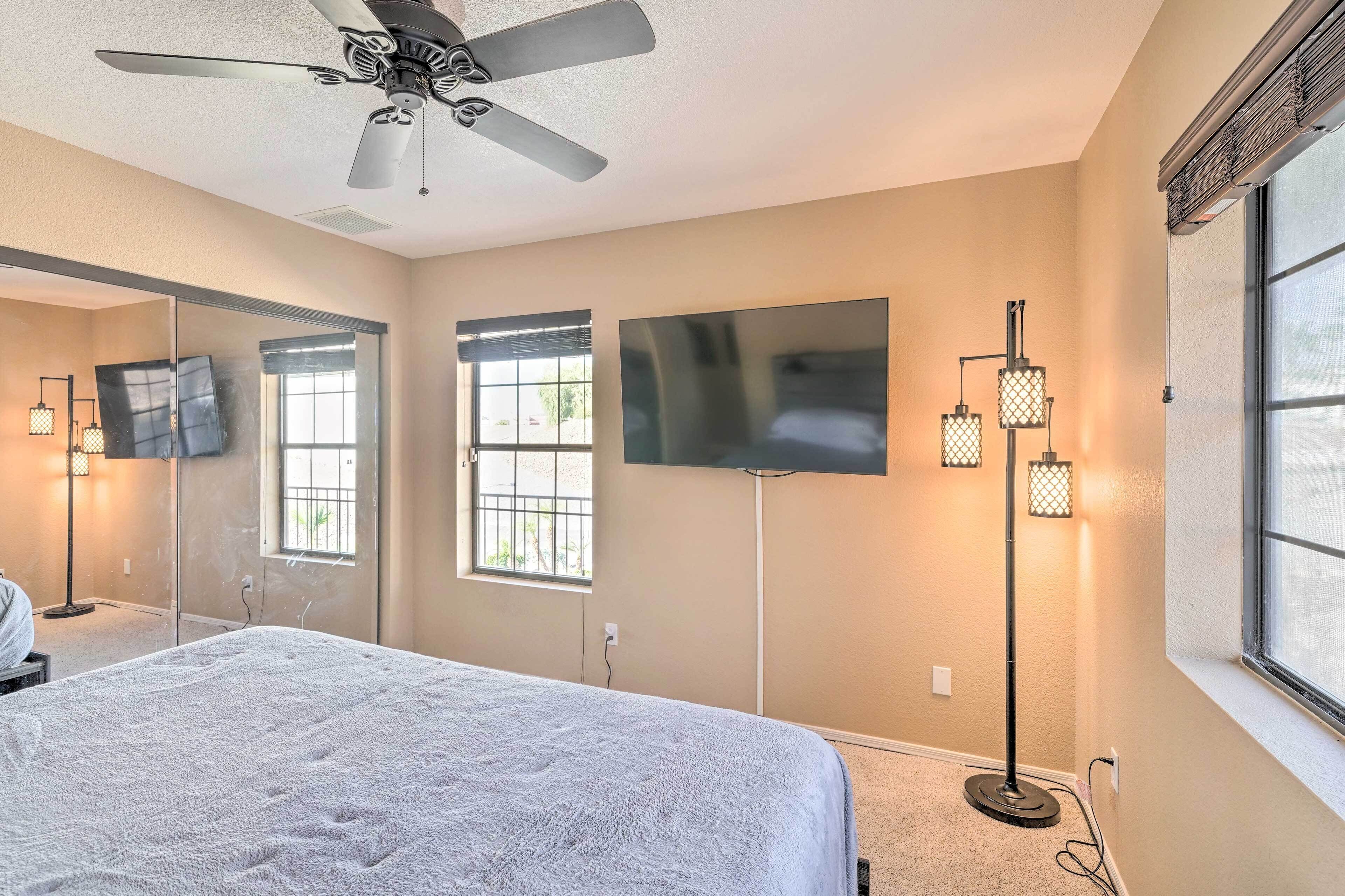 Une chambre à coucher avec un lit, un ventilateur de plafond, une télévision et une lampe sur pied.