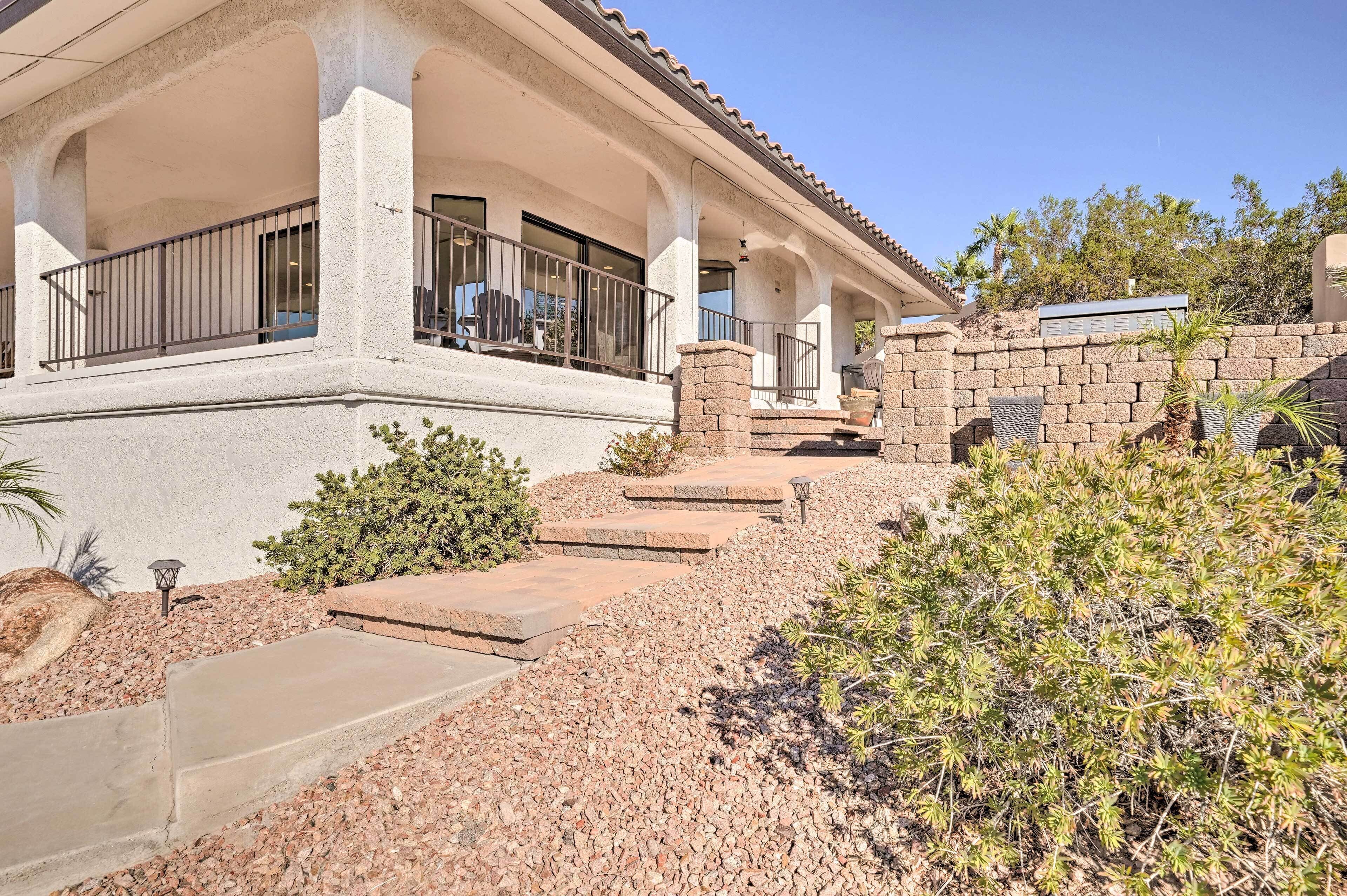 A house with a covered porch, stone steps, and a landscaped garden with shrubs and a palm tree.