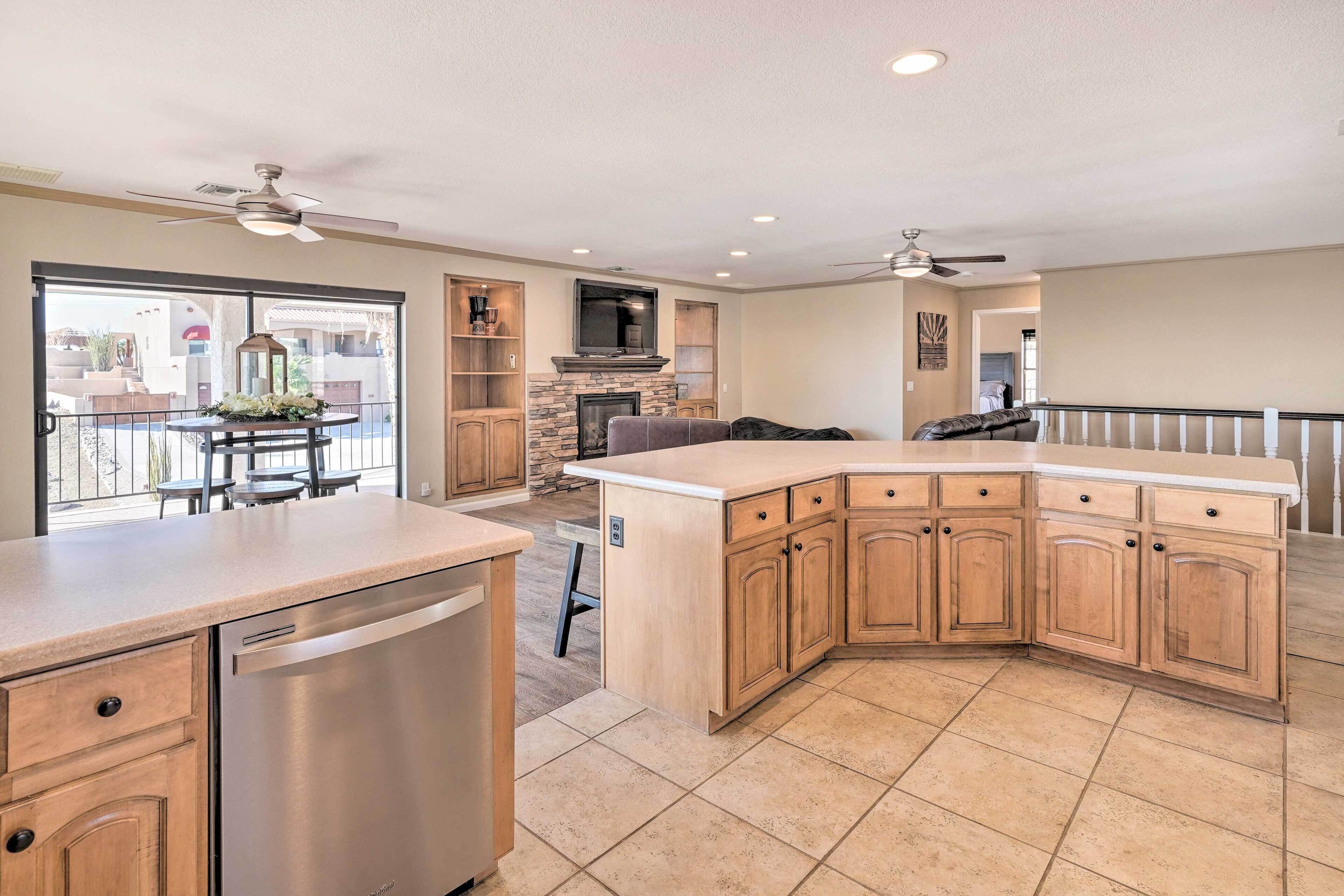 A modern kitchen with a dishwasher, a stone fireplace, and a dining area with a view.