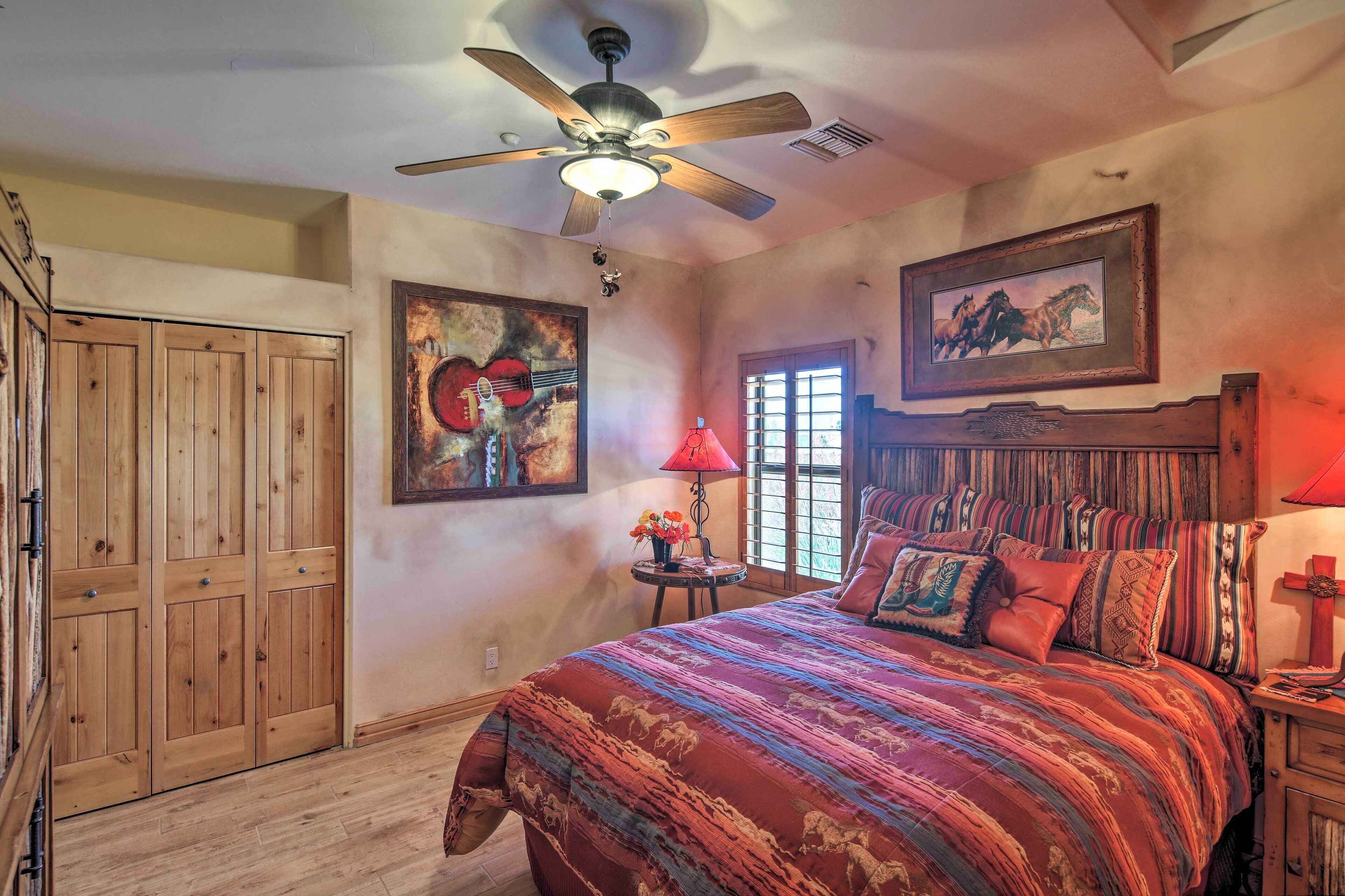 A bedroom with a large bed, wooden wardrobe, ceiling fan, and artwork on the walls.