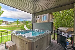 A hot tub and grill on a covered deck with a view of a residential neighborhood.