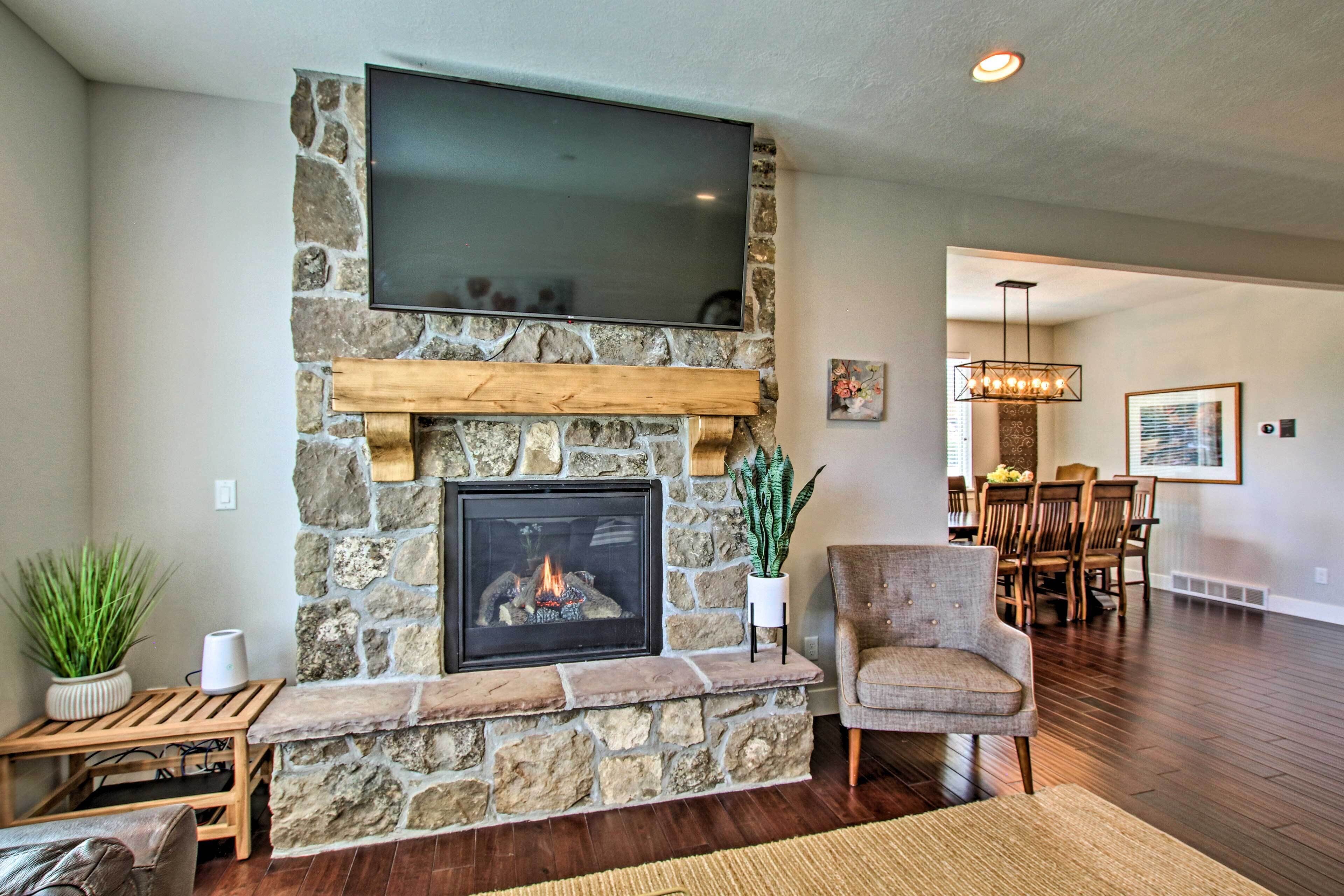 A living room with a stone fireplace, a flat-screen TV mounted above it, and a dining area in the background.