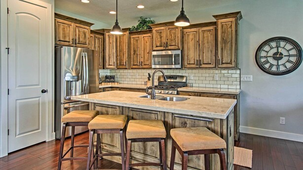 A kitchen with wooden cabinets, stainless steel appliances, a large island with bar stools, and a wall clock.