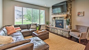 A living room with a stone fireplace, leather sofa, and a flat-screen TV mounted above it.