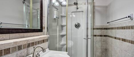 A modern bathroom with a glass-enclosed shower, a white sink, and a mirror above the sink.