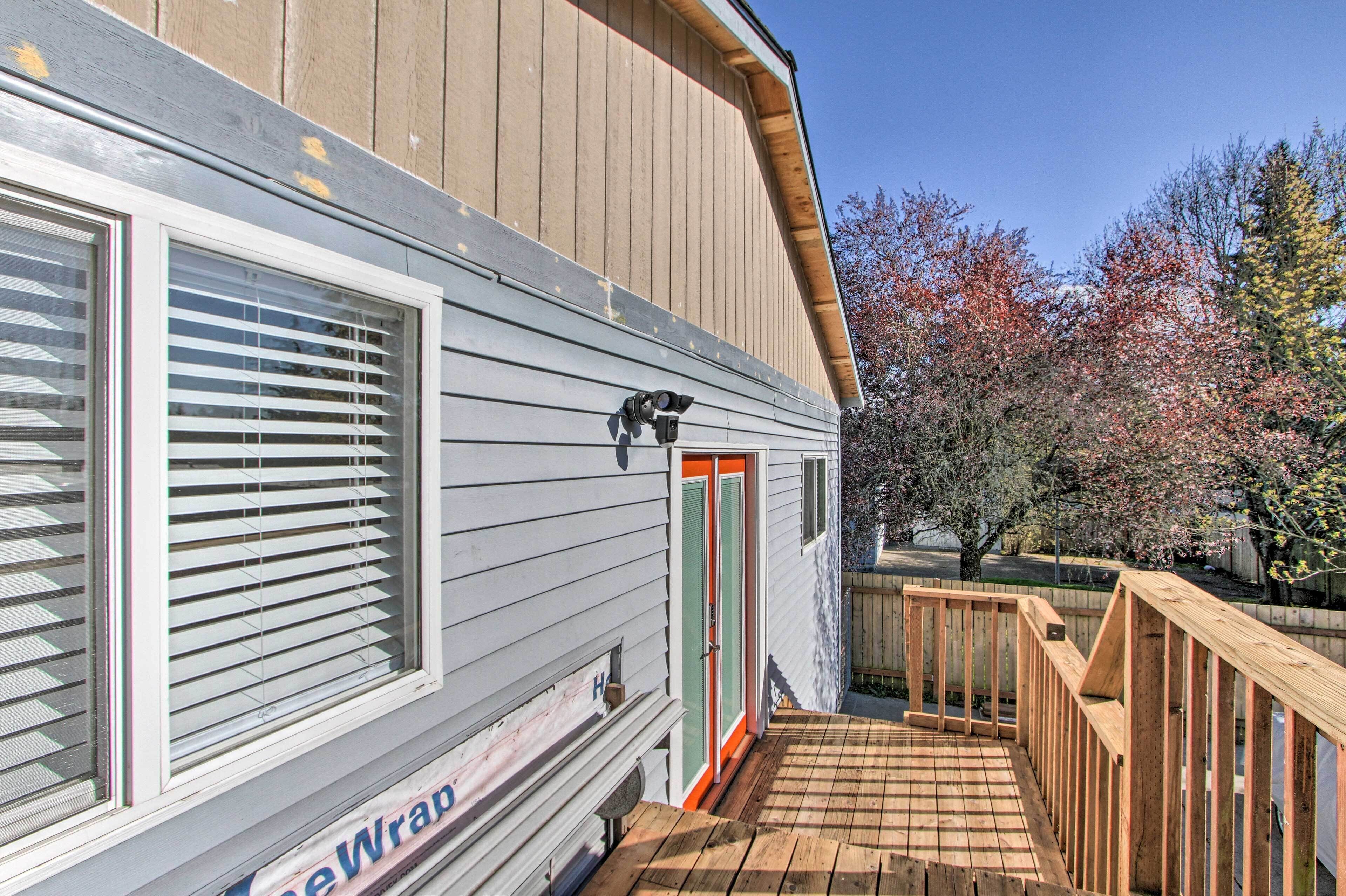 A mobile home with a wooden deck, a camera mounted on the exterior, and a door with a red frame.