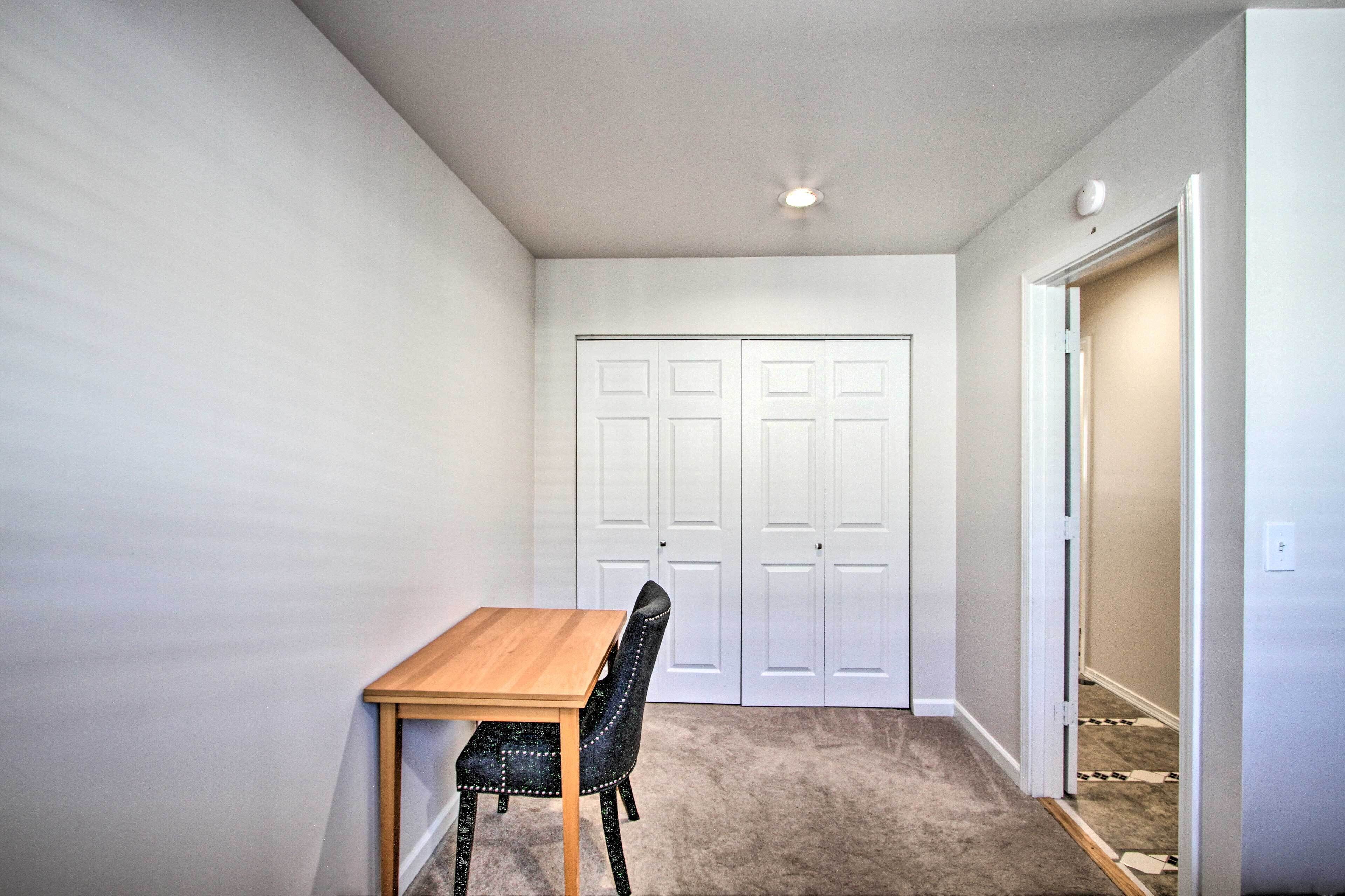 A room with a wooden table and a single chair, a white door, and a carpeted floor.