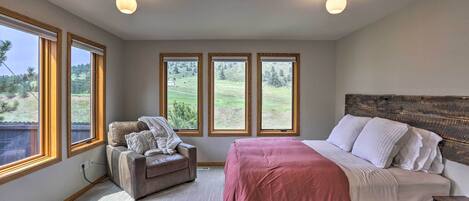 A bedroom with a bed, a chair, and large windows with a view of a green landscape.