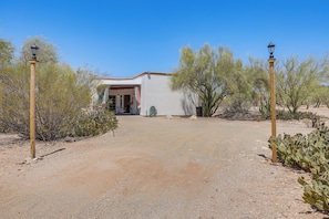 A desert landscape with a building entrance, two wooden lamp posts, and sparse vegetation. - Private Desert Garden: Cozy Tucson Casita (Tucson)