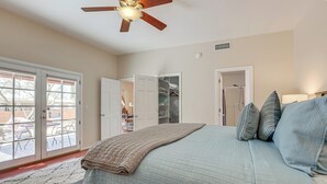 Une chambre à coucher avec un lit, un ventilateur de plafond, une grande fenêtre et un placard.