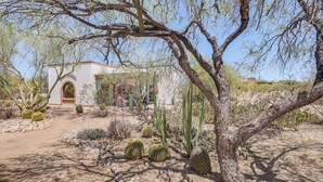 Un jardin désertique avec des cactus, un bâtiment doté d’une entrée en arc de cercle et un ciel dégagé.