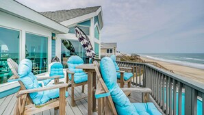 Une terrasse en bois avec des chaises bleues dotées de coussins et une vue sur la plage.