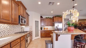 A modern kitchen with wooden cabinets, a granite countertop, stainless steel appliances, and a central island with bar stools. - Single-story San Bernardino Home w/ Valley Views! (San Bernardino)