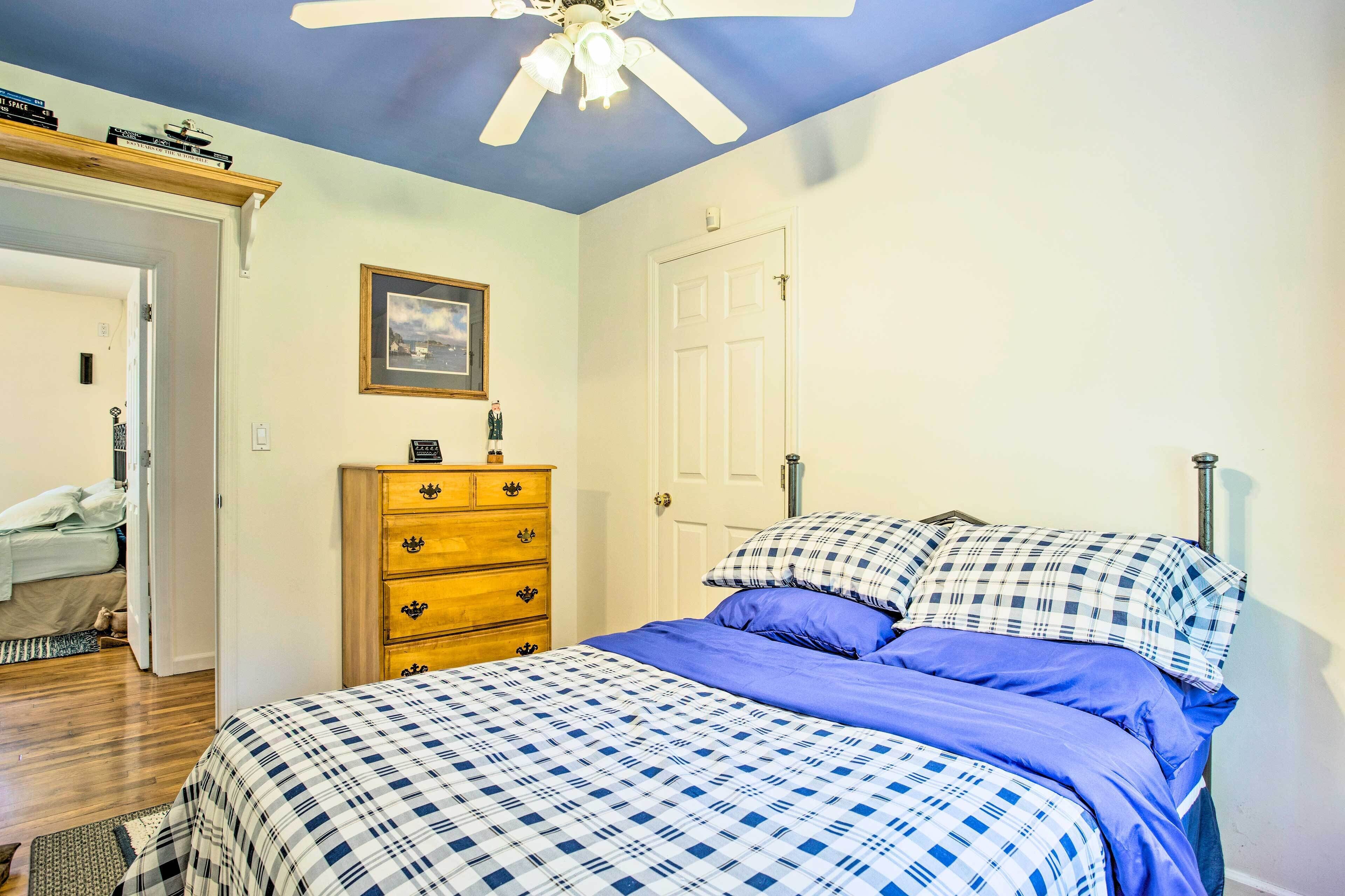 A bedroom with a bed, a wooden dresser, a ceiling fan, and a door.