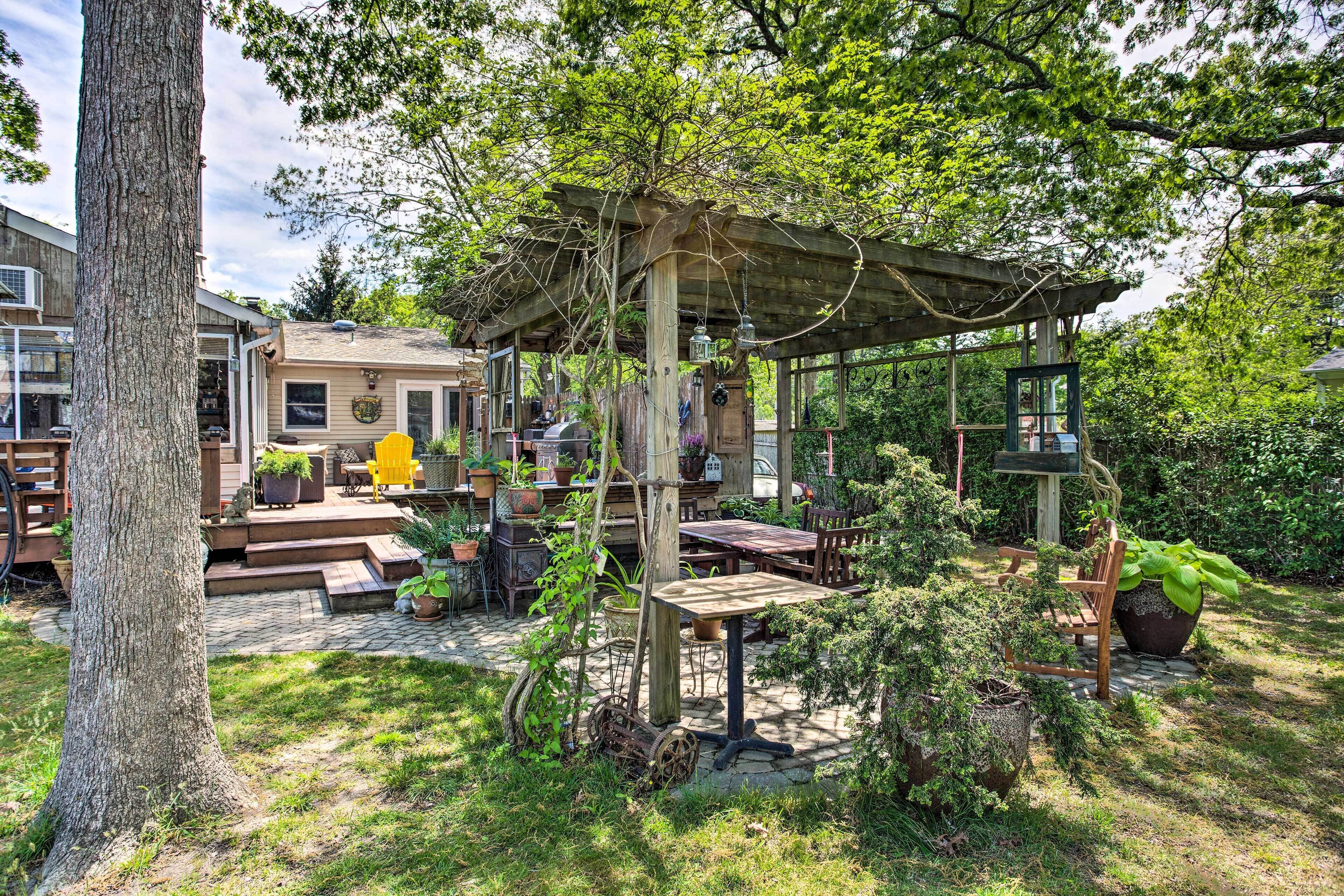 A covered outdoor seating area with a pergola, surrounded by potted plants and a stone pathway.