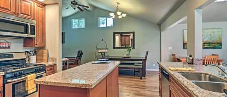 A kitchen with a central island, stainless steel appliances, wooden cabinets, and a dining area with a chandelier.