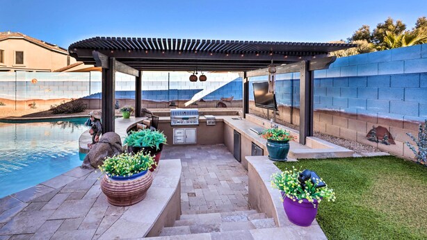 Une terrasse extérieure avec un espace barbecue, une piscine et des plantes en pot.