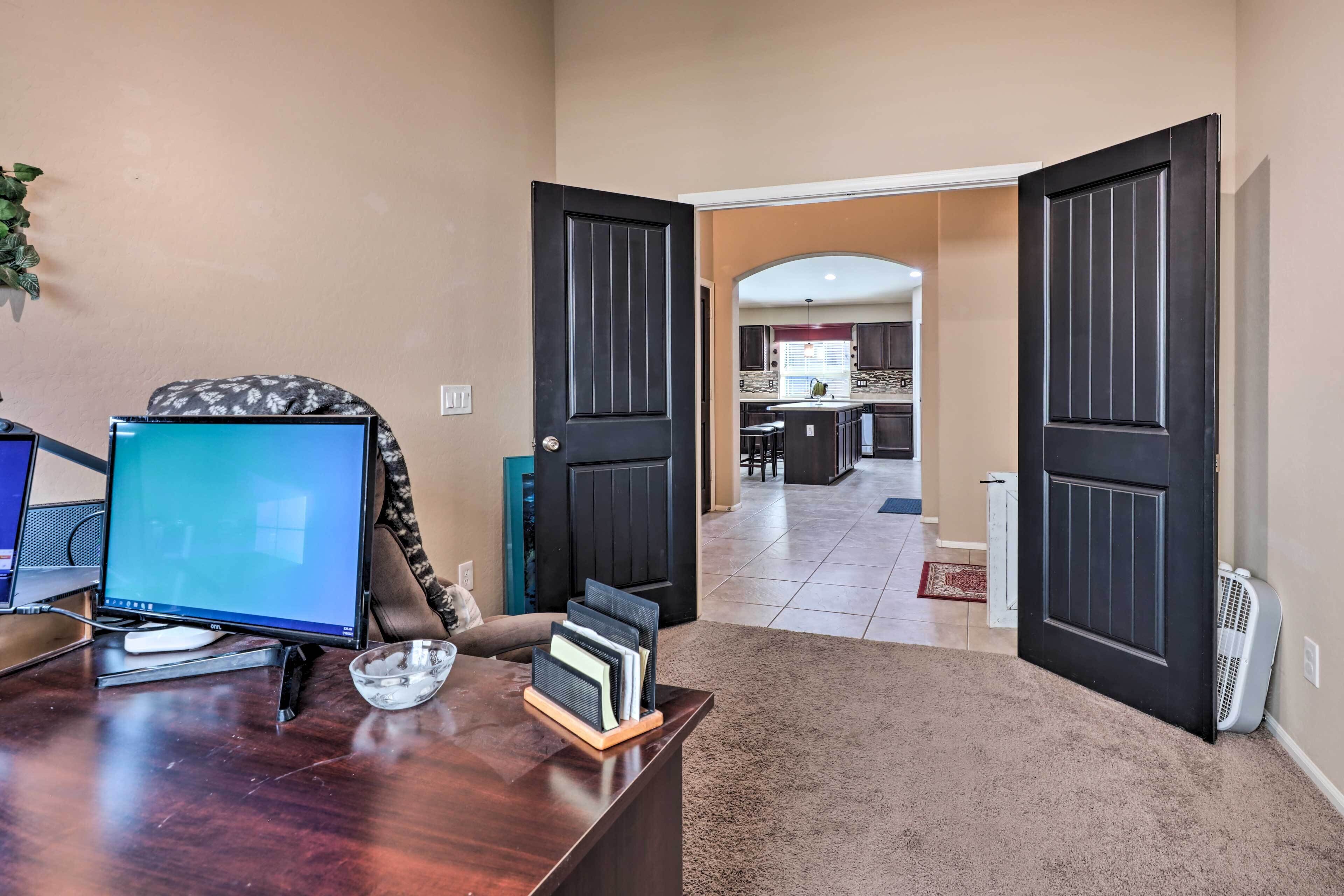 A home office with a desk, computer, and a view into a living area with a kitchen and dining space.