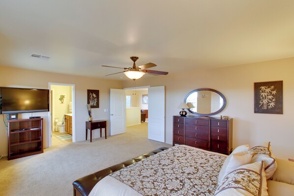 A bedroom with a bed, a dresser, a TV, a ceiling fan, and a bathroom in the background. - Patio & Community Perks! San Tan Mountain Retreat (San Tan Valley)