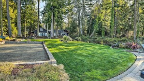 A well-maintained lawn with a stone pathway leading to a house surrounded by tall trees. - Mid-century Cabin w/ Deck & Puget Sound Vistas! (Hansville)