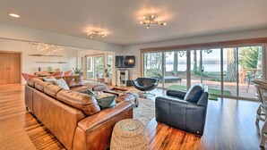 A spacious living room with a large leather sofa, a black armchair, and a flat-screen TV mounted on the wall. - Mid-century Cabin w/ Deck & Puget Sound Vistas! (Hansville)