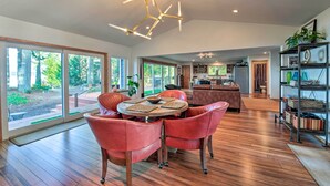 A spacious living area with a round table, red leather chairs, and a modern chandelier. - Mid-century Cabin w/ Deck & Puget Sound Vistas! (Hansville)