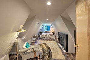 Um quarto de sótão aconchegante com cama, cadeira, mesinha e televisão.