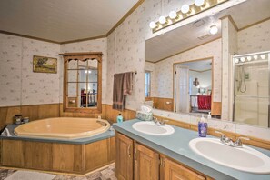 A bathroom with a large bathtub, two sinks, a mirror with lights, and wooden cabinetry. - Cedar Creek Lake Access: Retreat w/ Deck (Kemp)