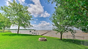 A grassy park area with a stone monument, a wooden walkway leading to a dock, and a body of water in the background. - Cedar Creek Lake Access: Retreat w/ Deck (Kemp)
