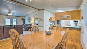 A spacious living room with a large wooden dining table, comfortable seating, and a kitchen area with wooden cabinets and a 'HOME' sign. - Cedar Creek Lake Access: Retreat w/ Deck (Kemp)