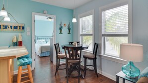 Une pièce comprenant une table à manger, des chaises, un petit tabouret, une lampe et une fenêtre avec des stores.