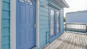 Une maison bleue avec une porte d’entrée, une fenêtre et une terrasse en bois.