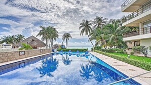Una piscina con sillas de descanso, palmeras y un edificio con balcones.