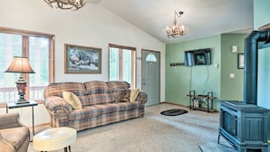A living room with a plaid sofa, a white ottoman, a fireplace, and a television mounted on the wall. - Cabin w/ Hot Tub, By Crater Lake Nat'l Park! (Klamath Falls)